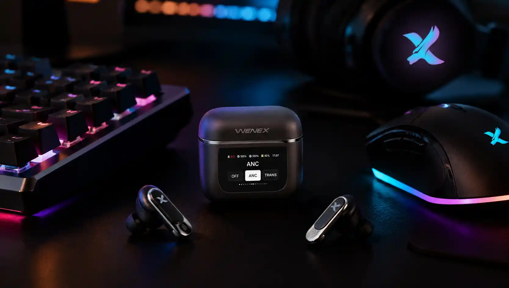 علبة WENEX Orbit V2 مفتوحة على مكتب ألعاب بجانب لوحة مفاتيح مضاءة وفأرة وسماعة، وشاشتها الذكية تعرض تحكم ANC.